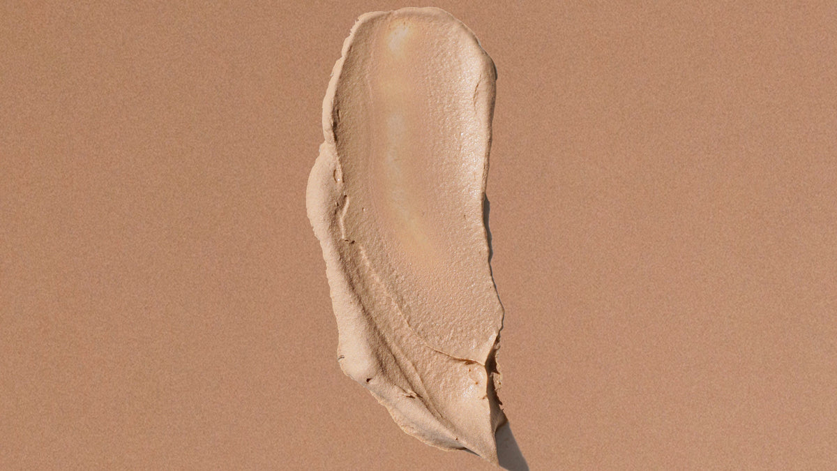 A textured smear of beige liquid spf on a solid, warm tan background.