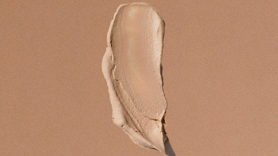 A textured smear of beige liquid spf on a solid, warm tan background.
